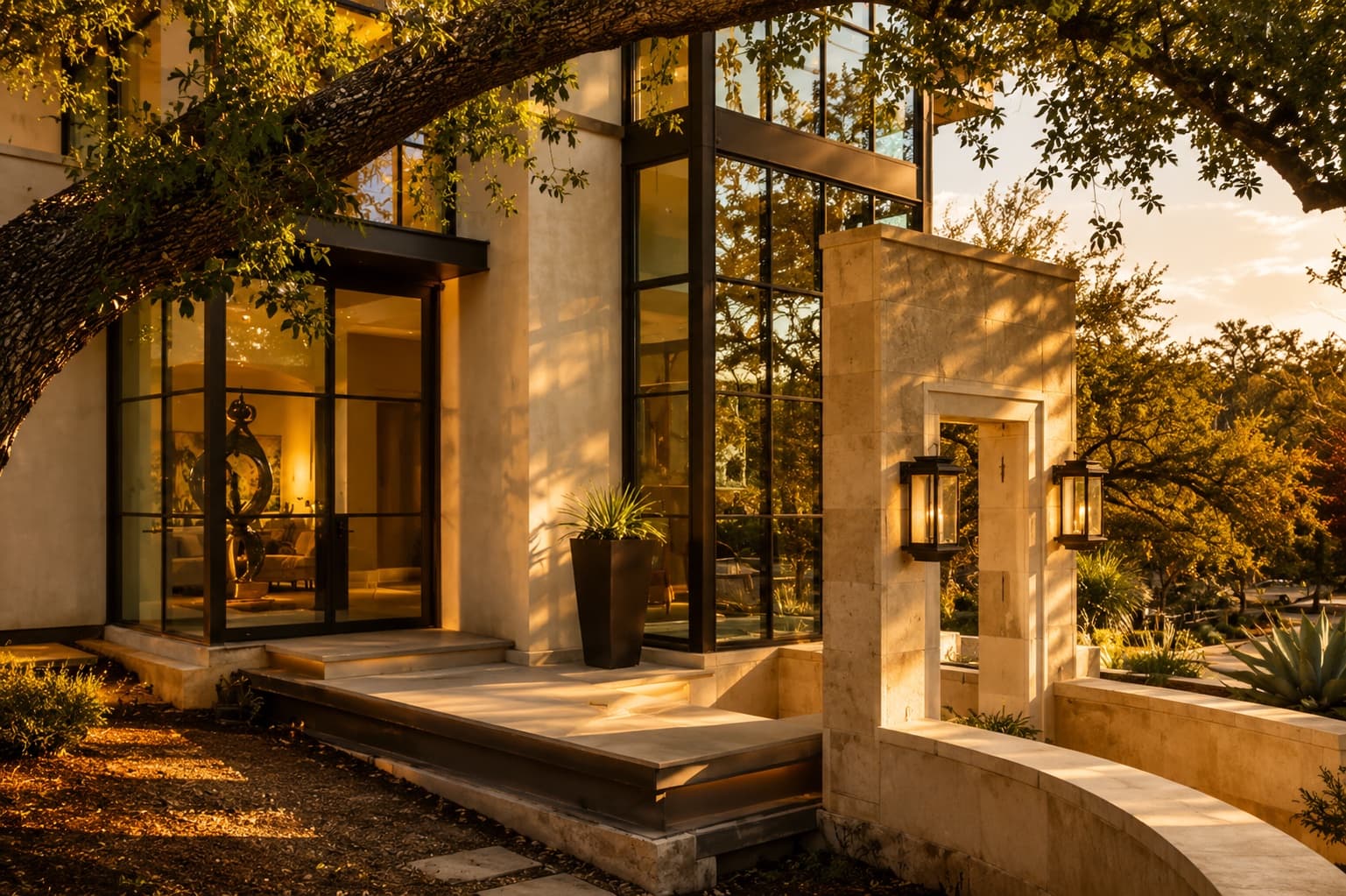 A stately West Austin home of stone, steel, and glass framed by a live oak at golden hour in Tarrytown